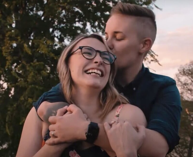 a person hugging their partner from behind and kissing their head 