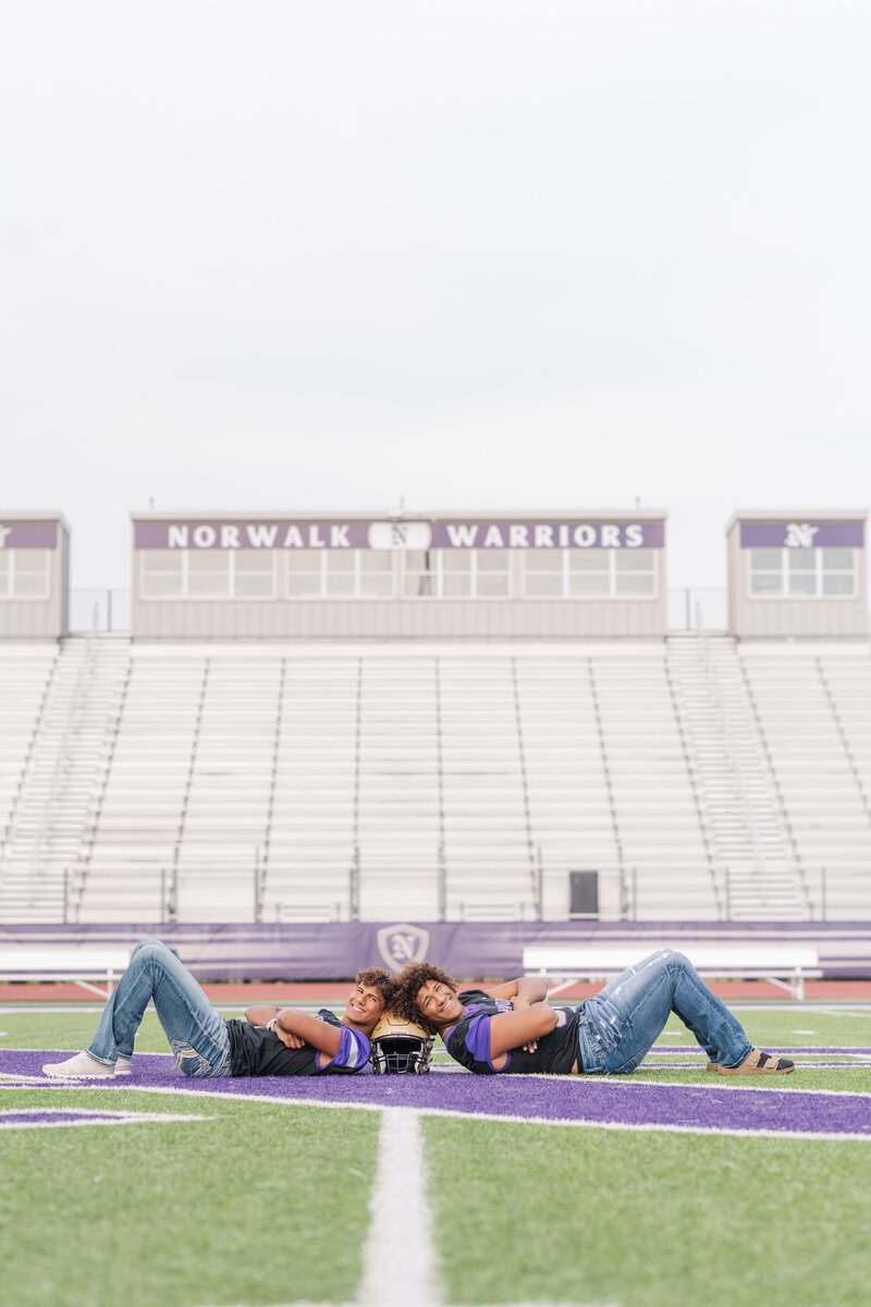 two twin brothers laying on a football field while wearing their jerseys