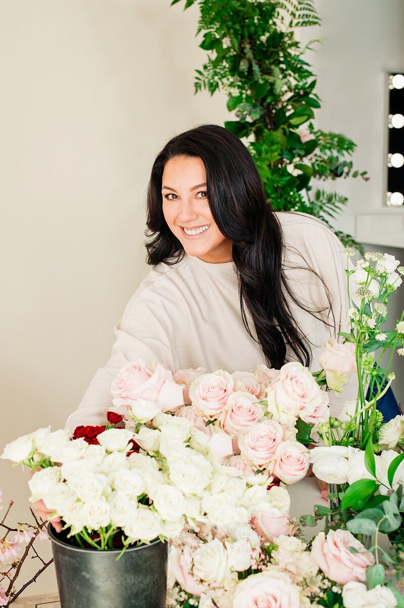Pink and white roses in the front of a florist as she selects stems and smiles at the camera