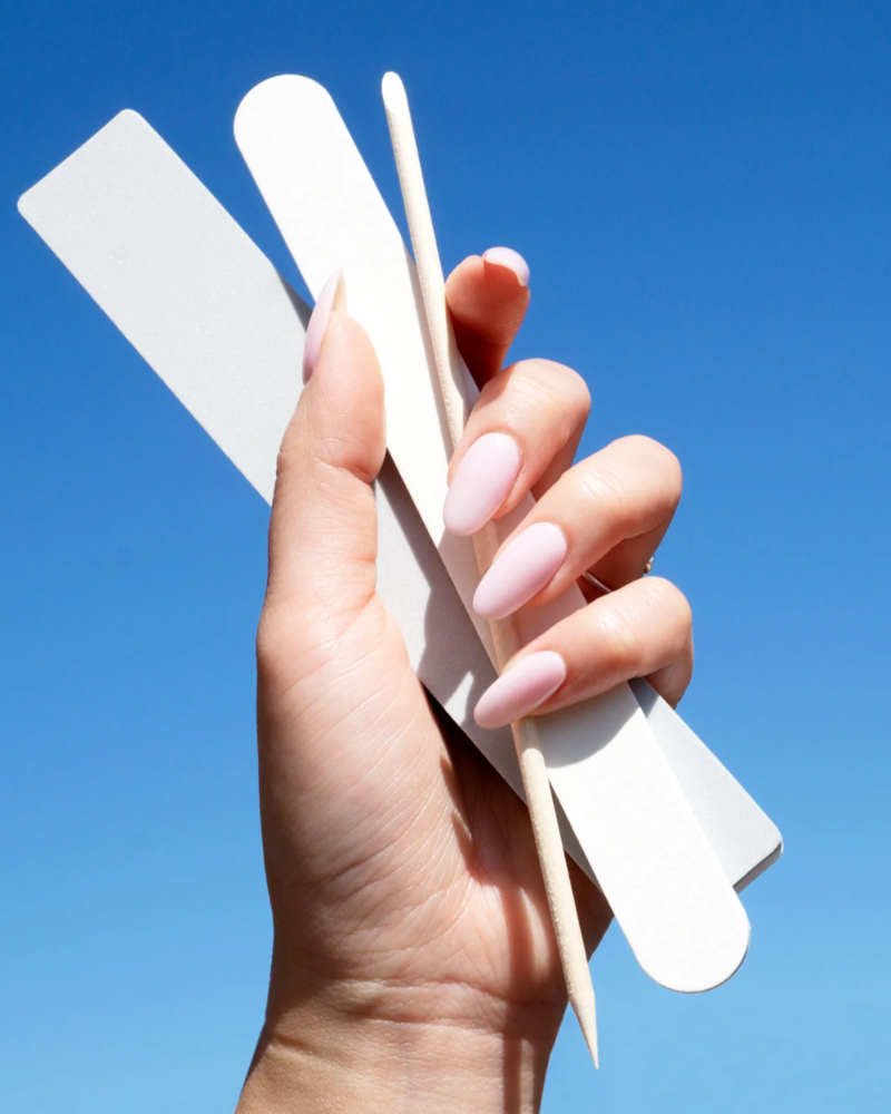 Hands with pink fingernails holding nail files and manicure supplies in front of a blue background