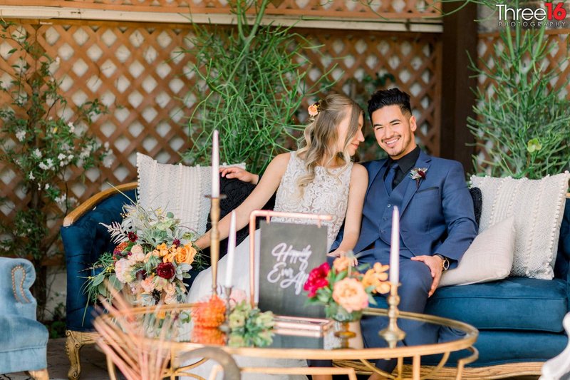 Bride and Groom sit together on an outdoor patio couch with smiles on their faces