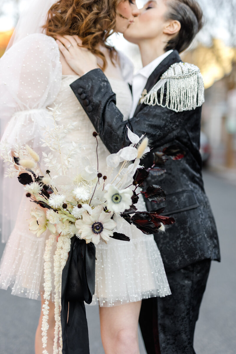 close up of queer bride holding their bouquet in front while embracing and kissing nonbinary partner in the street in Georgetown DC 