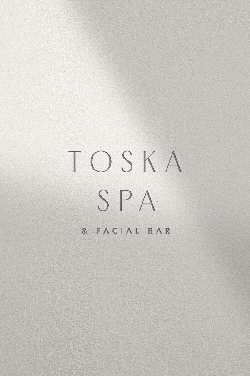 Toska Spa logo embossed on soft light-textured background, conveying simplicity and elegance