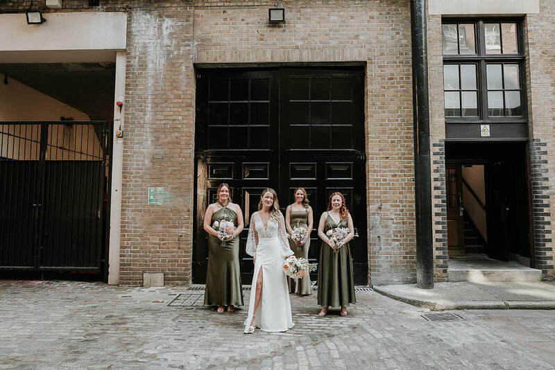 Bride and bridesmaids in green dresses posing outside The Truman Brewery. London