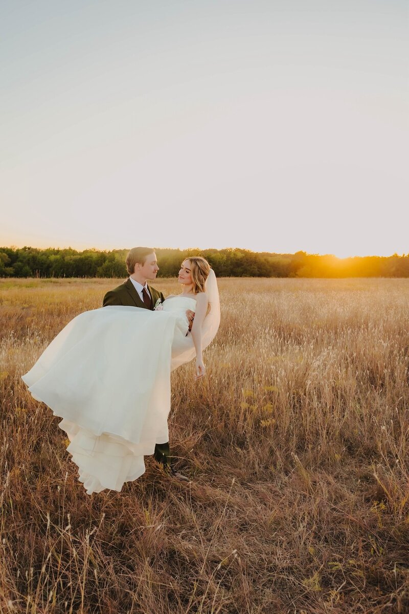groom holding bride in field at oklahoma wedding