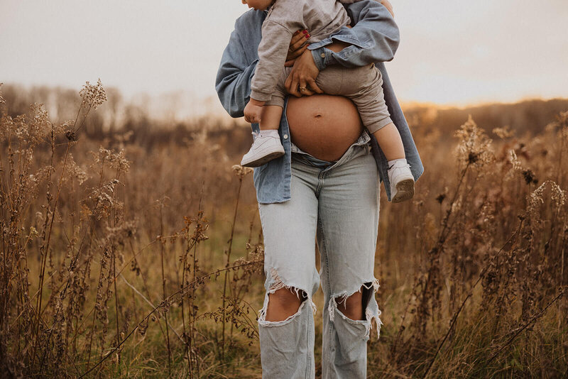 Expecting mother with open jeans and denim shirt showing her belly holds her toddler son