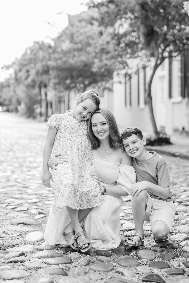 A black and white family photo of a Dallas/Fort Worth TX  family photographer holding her 2 children while posing in the middle of a stone road.