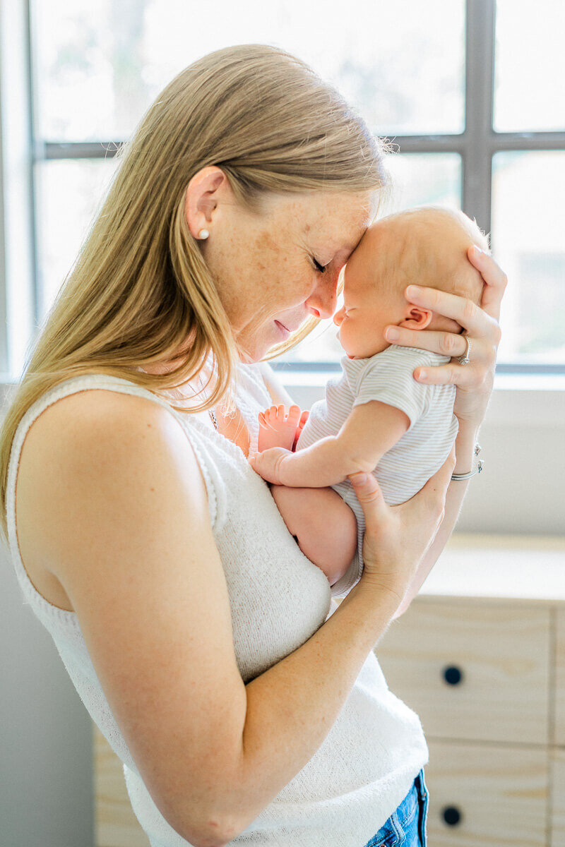 A mother stands with her newborn facing her, leaning her forehead against his while captured by an Austin newborn photographer.