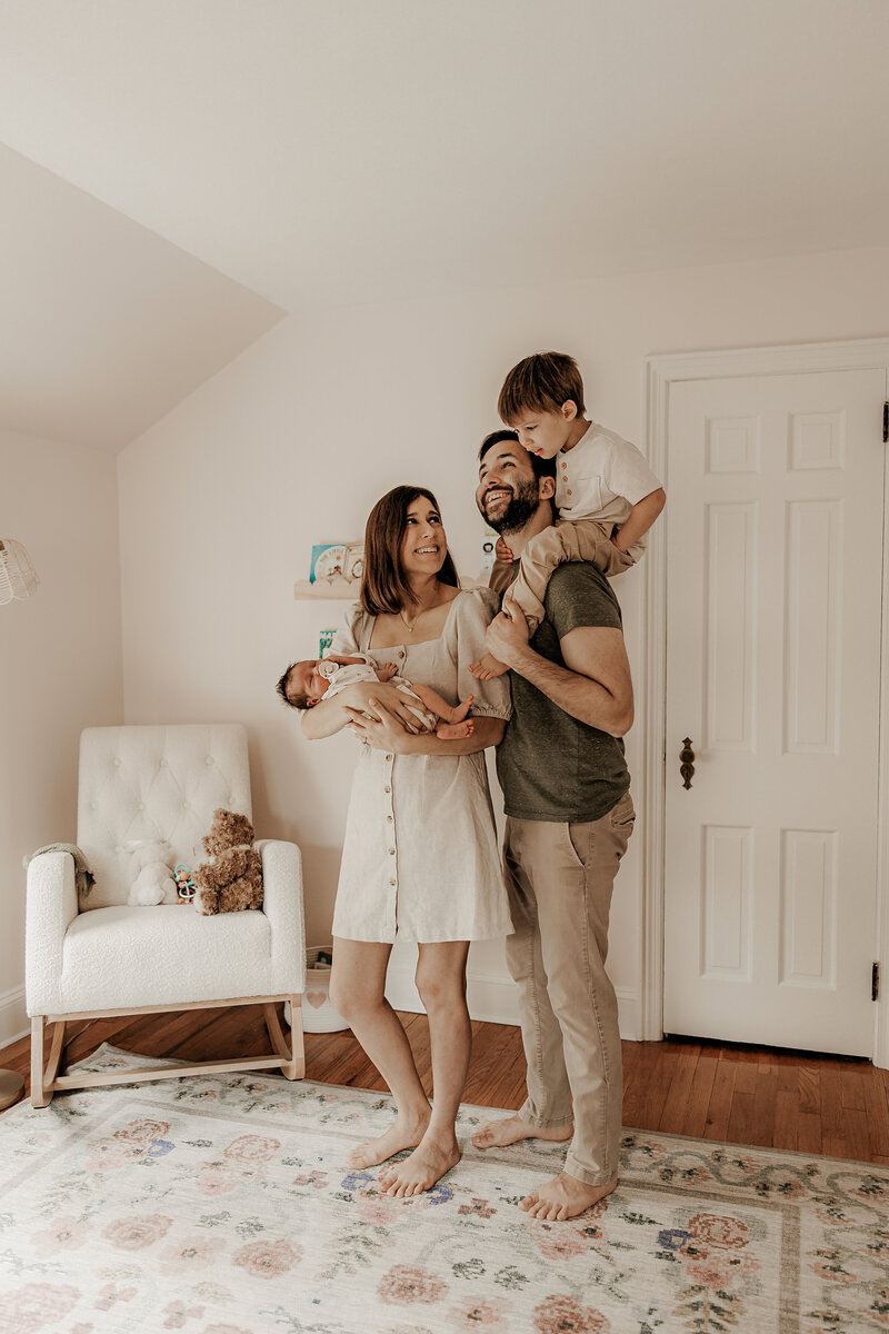 Cozy in-home newborn photography session in Morristown, New Jersey featuring parents and older brother lovingly holding their baby in soft natural light gazing lovely at each other.