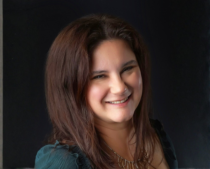 Kellye Mazzoli leaning against a brick column, wearing a navy blazer, rust-colored blouse, and jeans, smiling confidently with a relaxed and approachable pose - City Boss Coaching-Kellye Mazzoli