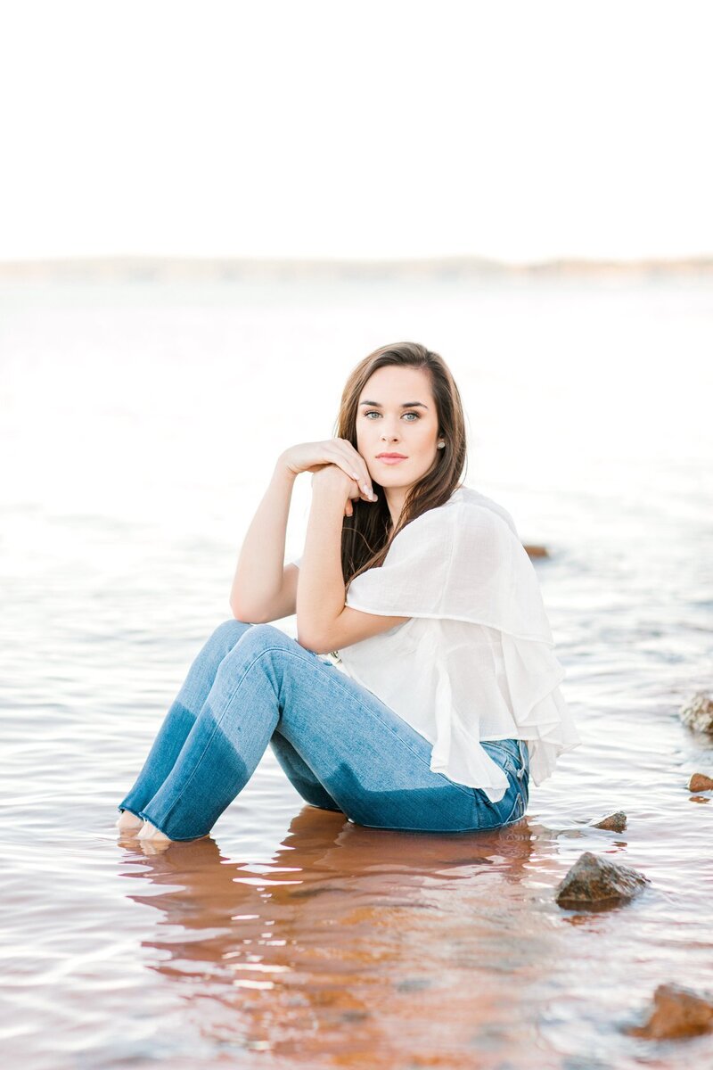 dark haired girl wearing jeans sitting in water looking at the camera