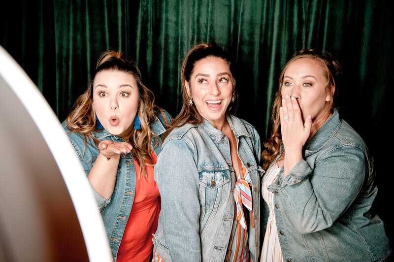 Three attendees pose playfully at a photo booth with green curtain backdrop at a Phoenix corporate event, photographed by MISGIF.