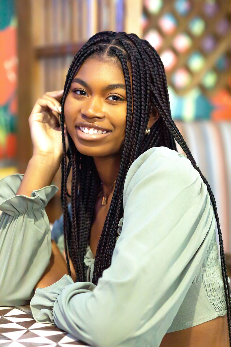 Senior girl with braids wearing sea green long sleeve crop top and black destructed jeans posing casually sitting at a table