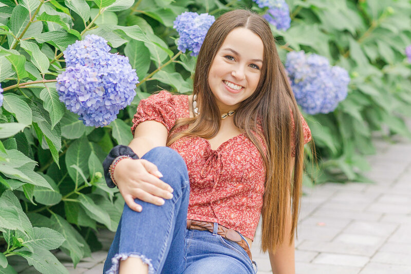 High school girl sitting in front of hydrangeas during Warrenton, VA senior pictures