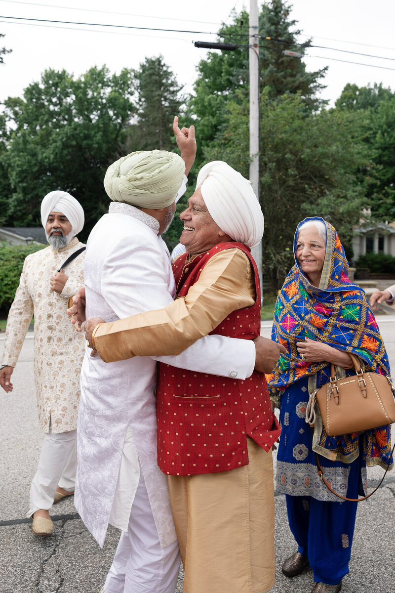 Two older Indian men embrace on their childrens wedding day.