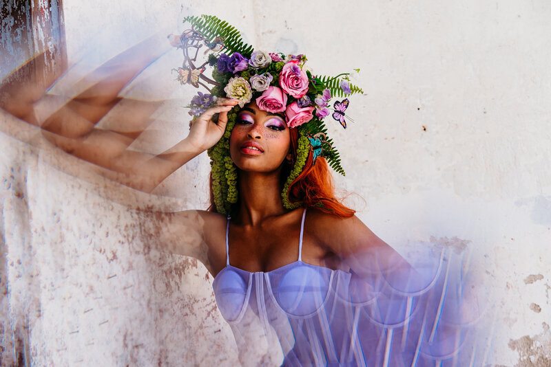 a creative picture of a model with a floral headpiece on top of her head posing on a wall