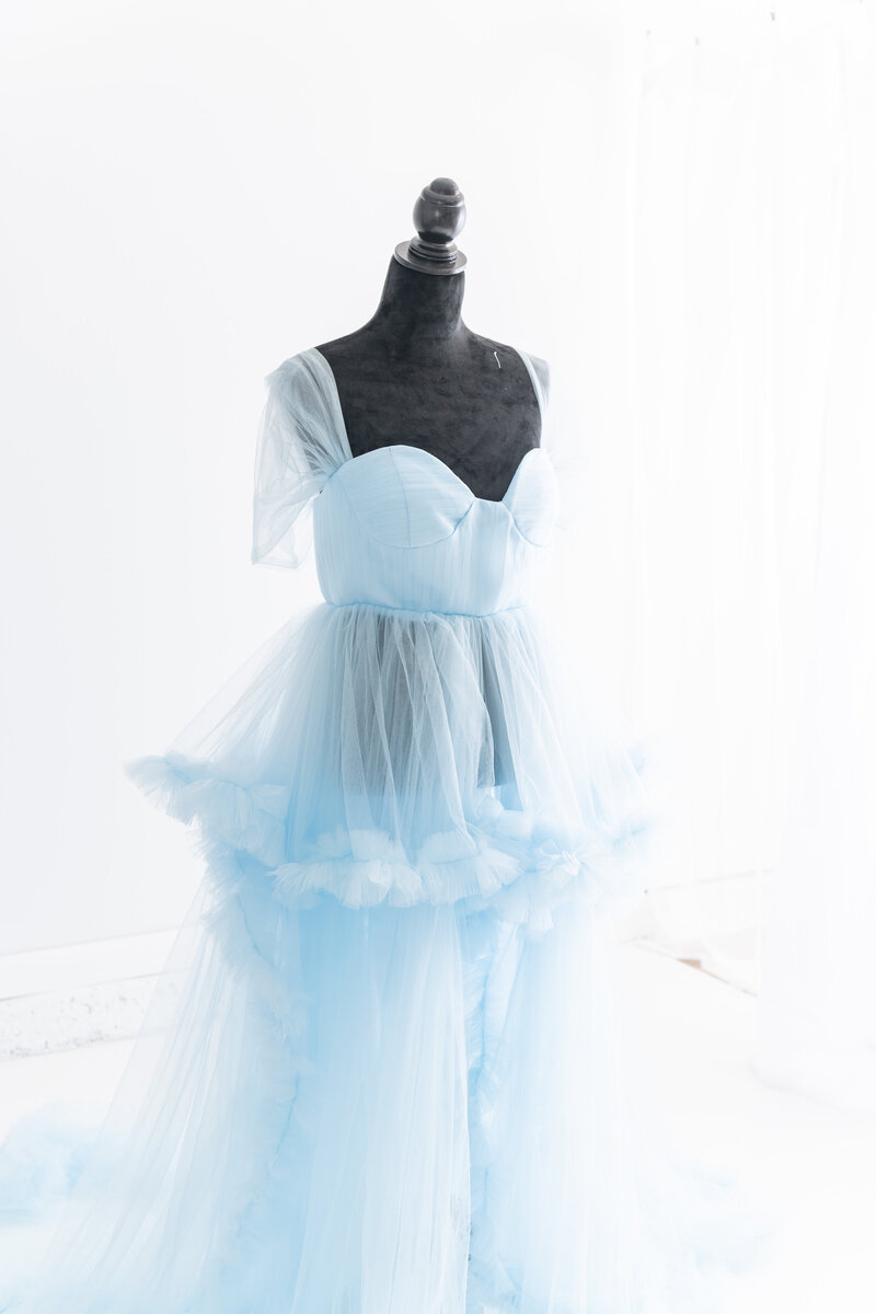 A sheer blue tule maternity gown hangs on a black mannequin