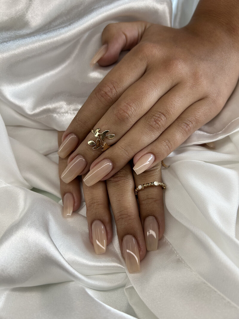 Close-up of a client’s hands showcasing elegant nude French acrylic nails with a glossy finish, done at Blushed Miami.