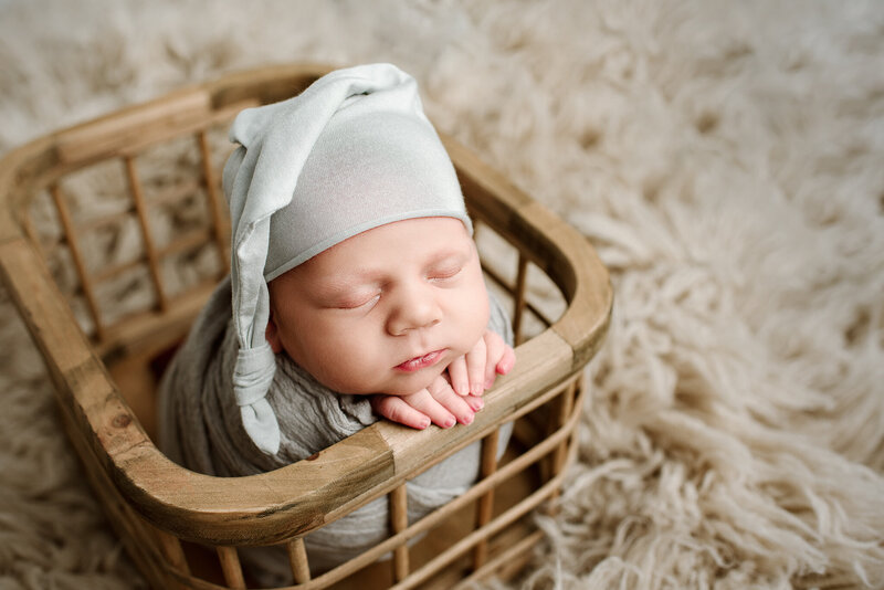 Newborn boy posed in wooden crate with gray sleepy cap  in Jacksonville Beach, FL.