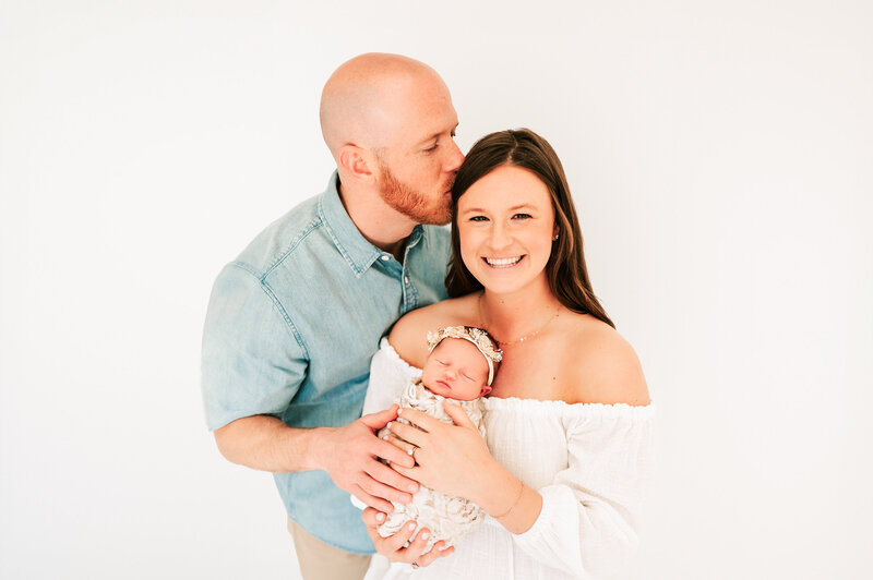 Newborn photography of parents holding sleeping baby girl in all white newborn studio in Springfield MO
