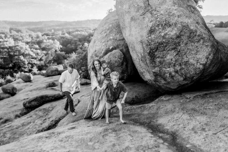 Oldest son holds mom's hand and walks with her and his family up rocks with Kansas City Family Photographers.