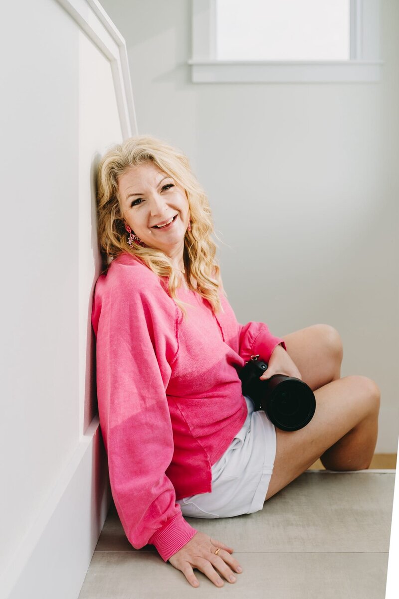 Photographer Kellie Llewellyn wearing a pink shirt and holding her camera