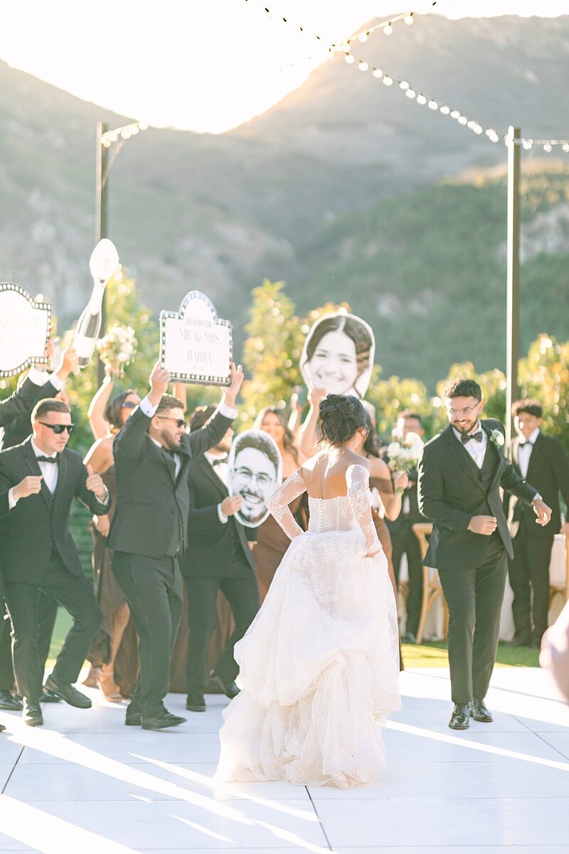 Bride and groom dancing among their wedding party during their grand entrance on a white dance floor at Rancho Guijito Vineyard, the light pouring through the mountains in the background.