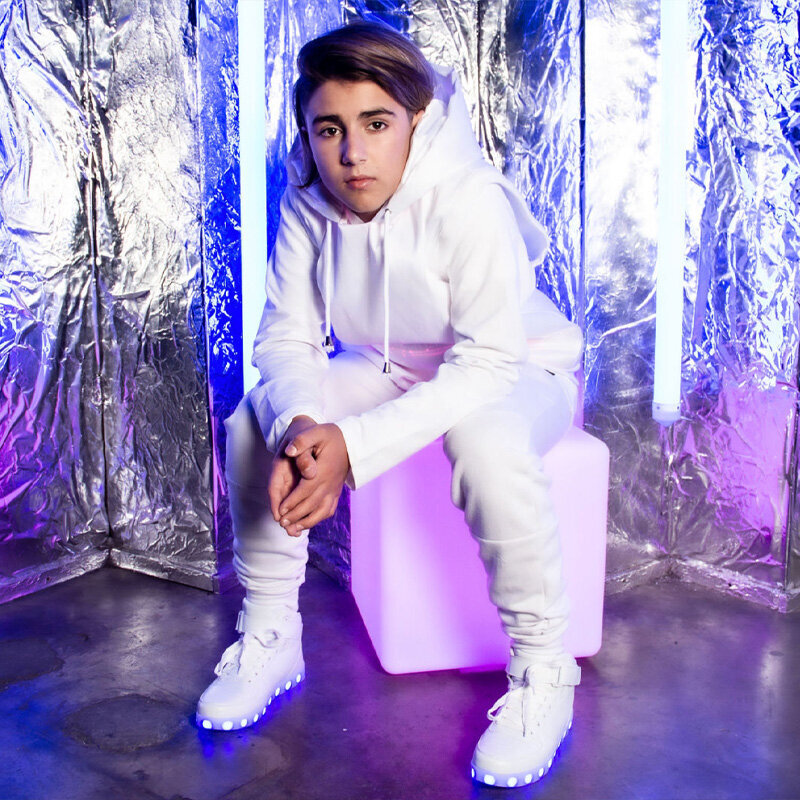 Dominique Ilie personal branding photo wearing white track suit sitting on white cube against metal wall with purple neon lights