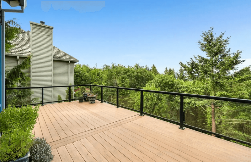 A large wooden balcony with black rails and a view of trees.