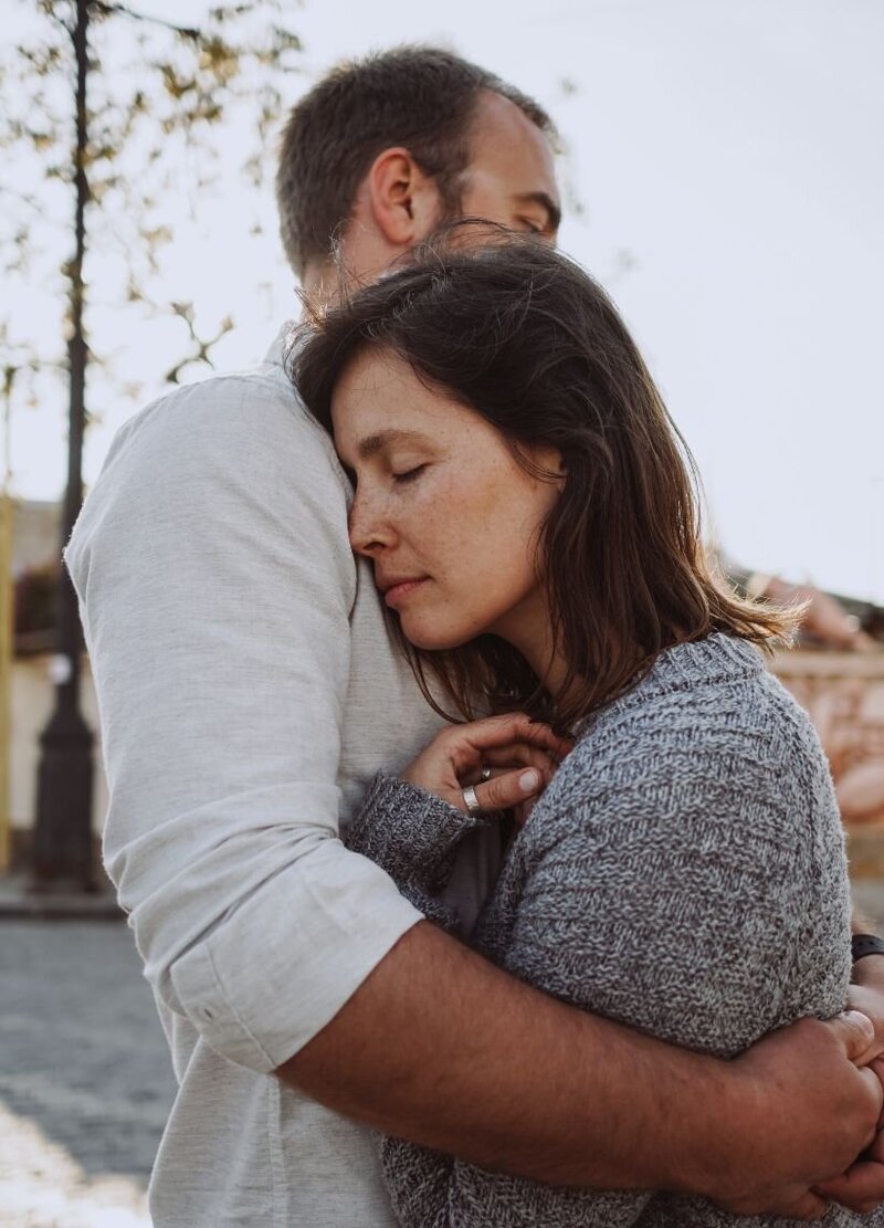 A man hugging his wife and a wife is with her eyes closed. This can represent a couple who was in the aftermath of infidelity and managed to heal and rebuild trust using Relationship Experts roadmap to healing from infidelity.