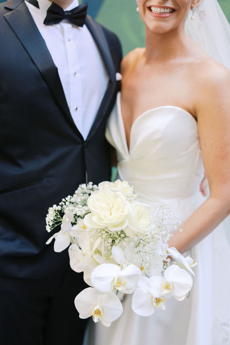 Bride holding elegant floral bouquet stands close to groom in black tie suit