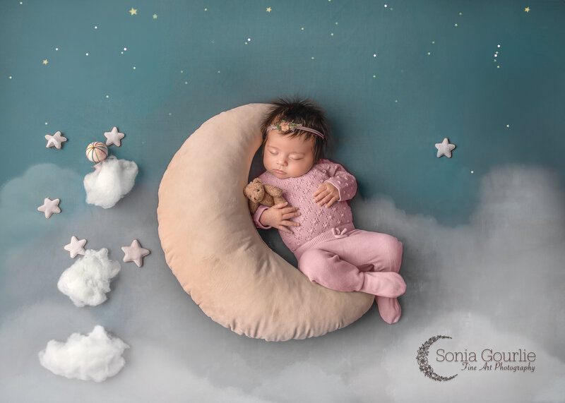 "Newborn baby peacefully sleeping in a moon and stars-themed setup, with soft lighting and whimsical props, captured at Sonia Gourlie Fine Art Photography in Ottawa."