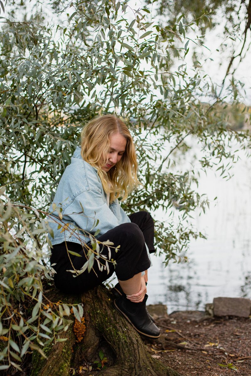 mielen paremminvoinnin ja kehomieliyhteyden valmentaja istumassa puunrungon päällä puunlehtien keskellä järven rannalla