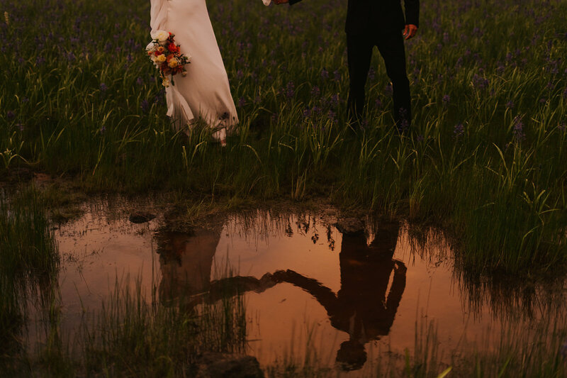 A pond that shows the reflection of a couple holding hands and looking at each other.