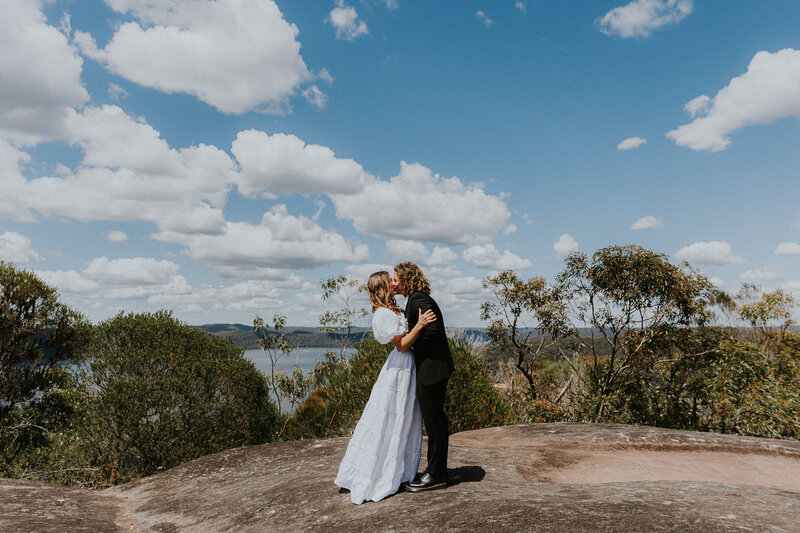 A couple kissing on a rock overlooking a grand vista of Hawkesbury River on the Central Coast during their Elopement with Underatreehouse Photography, the best elopement photographer in Australia