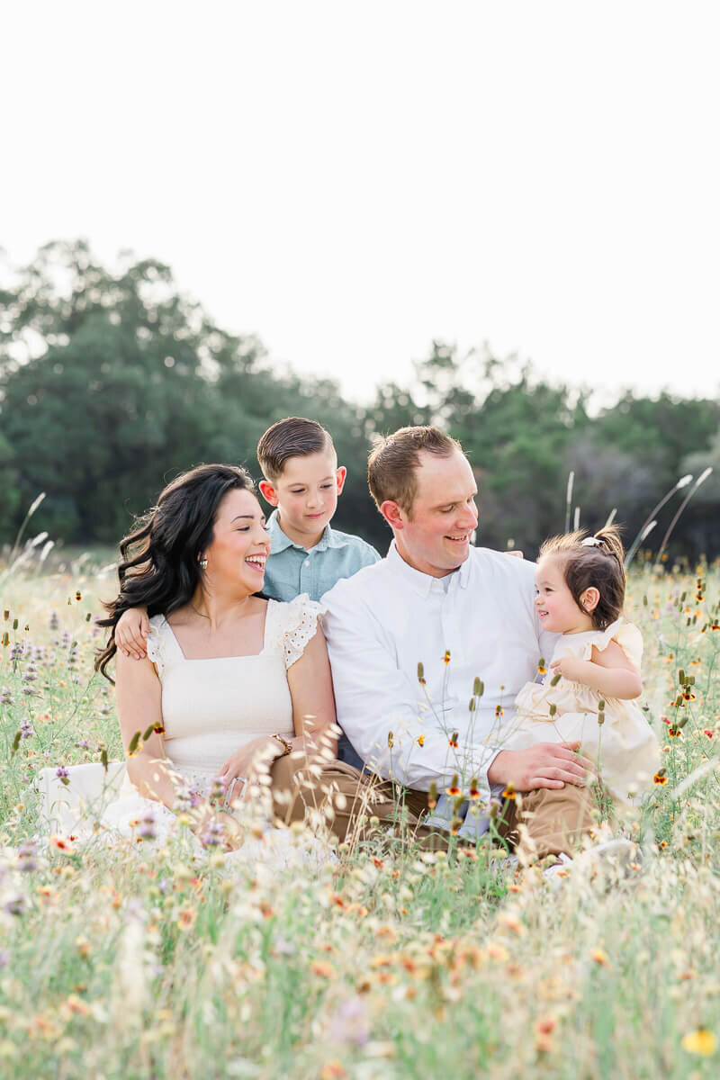 a family with a young boy and a toddler girl sit in a field of wildflowers, captured by an Austin family photographer.