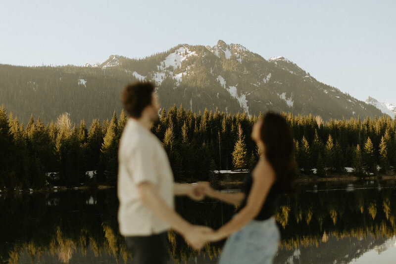 A couple holding hands with a beautiful mountain peak in the distance at Gold Creek Pond in Washington.