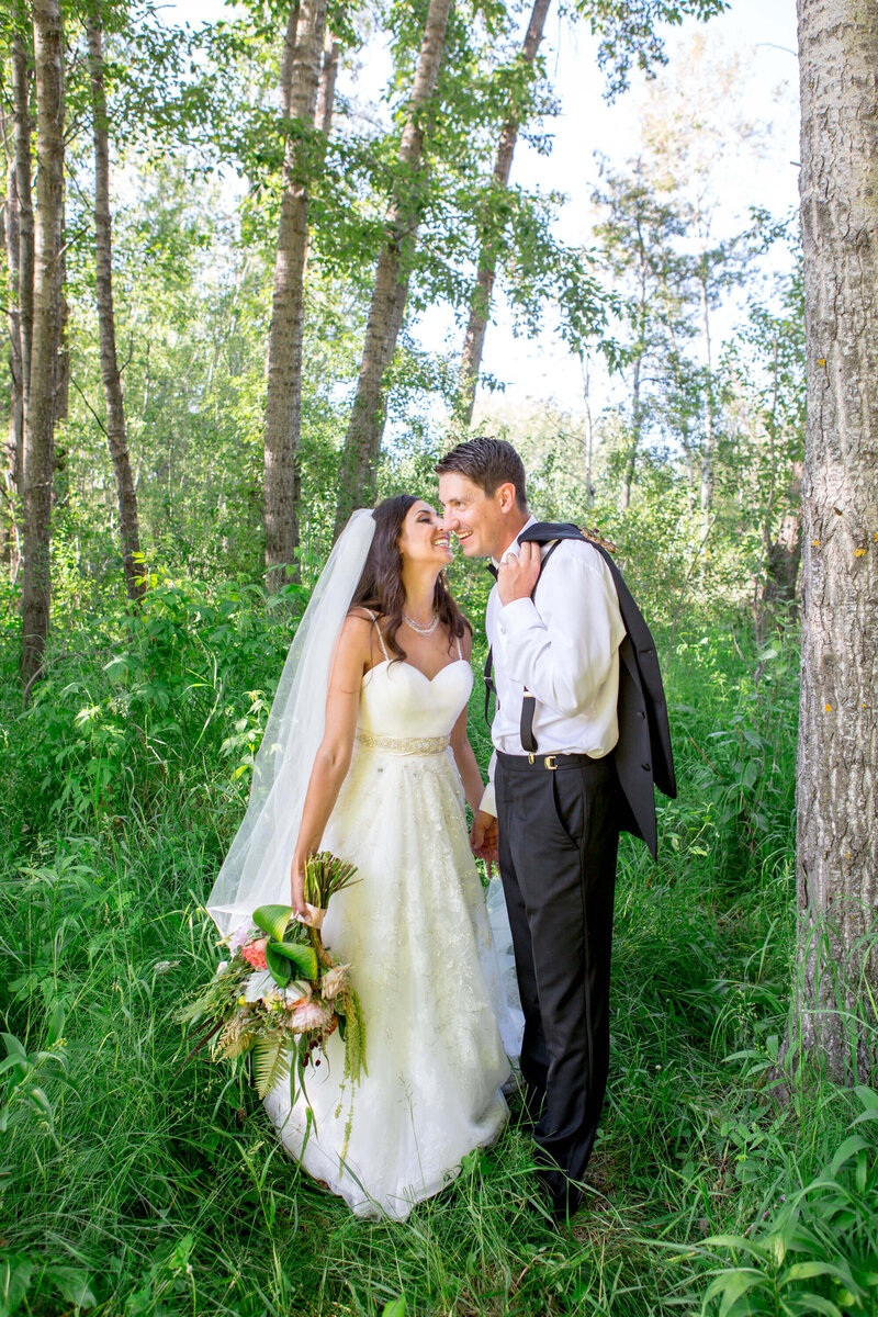 bride kisses groom on cheek in the forest