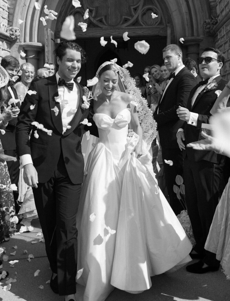 bride and groom laugh, wedding exit, Michigan petal toss at cathedral, lace trim mantilla veil, white rose petals