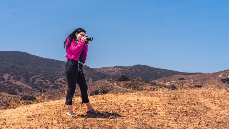 Utah branding photographer capturing a portrait in the desert foothills near Salt Lake City, wearing a vibrant pink fringe jacket while photographing the landscape. Editorial, high-end branding photography by Moonlit Photo in the mountains of Utah.