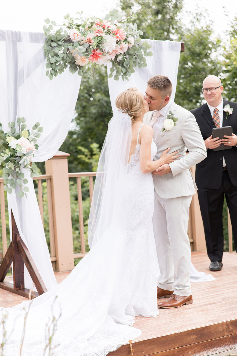 Bride and groom first kiss under floral arbor