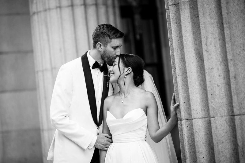 San Francisco Bay Area wedding photographer captures intimate black and white moment as bride and groom embrace outside historic Julia Morgan Ballroom with classical columns