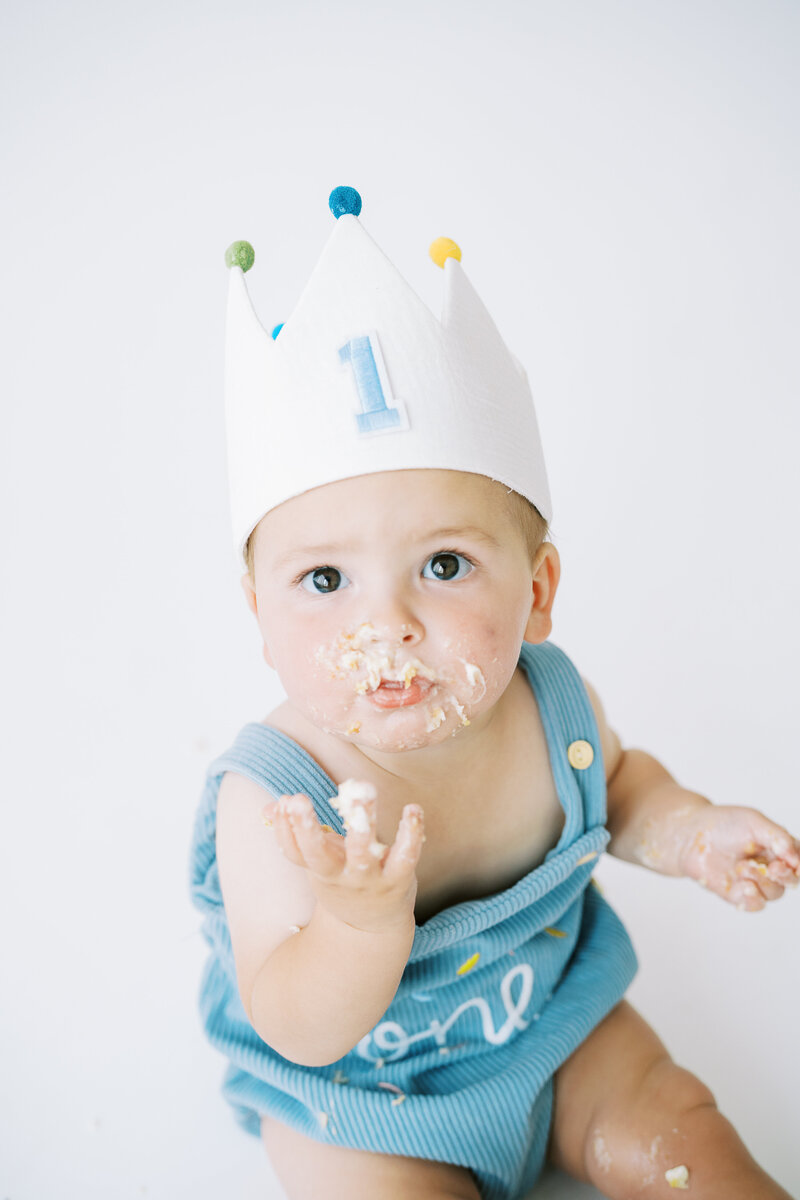 a baby with cake and frosting on his face and fingers