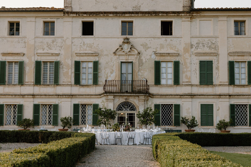 A small wedding reception table set up in a garden in front of a mansion 
