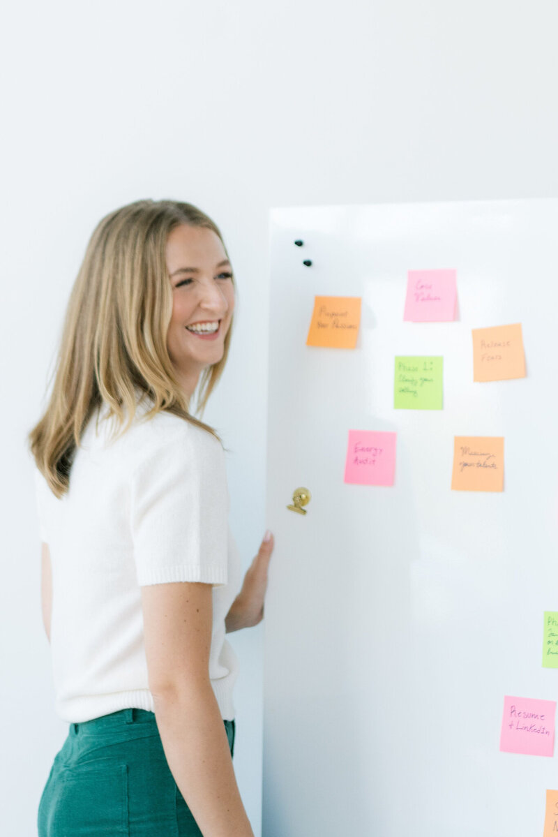 Audrey smiling and standing in front of a whiteboard covered in colorful sticky notes