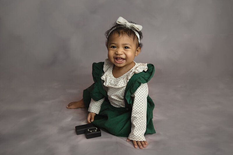 A young toddler girl smiles big while playing in a studio in a green dress