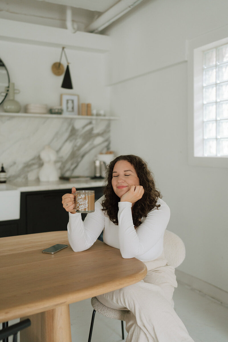 Morgan carrying a laptop and coffee cup by a table