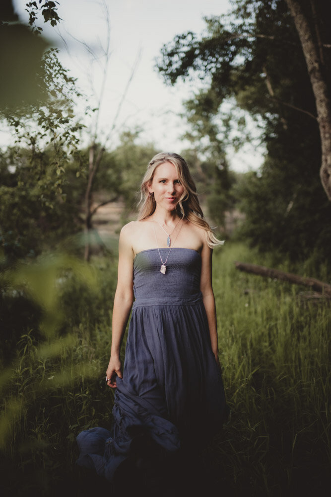 Caroline Weiss standing in a forest surrounded by trees, reflecting peace, grounding, and connection with nature.