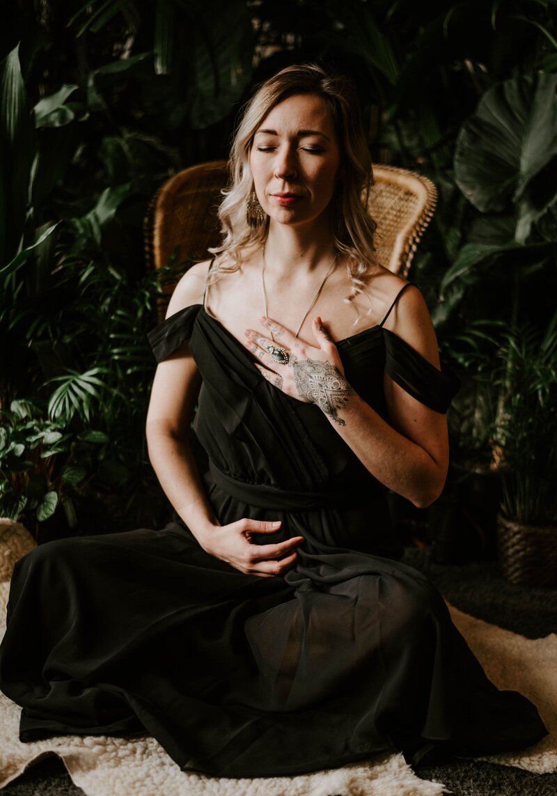 Shae Savage sitting quietly in a black dress meditating