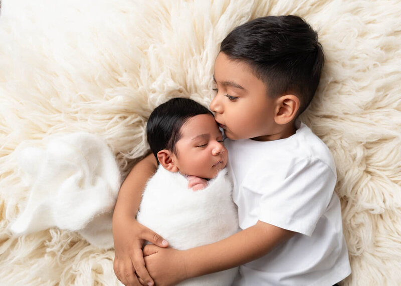 sibling-kissing-newborn-on-white-fur-blanket-7